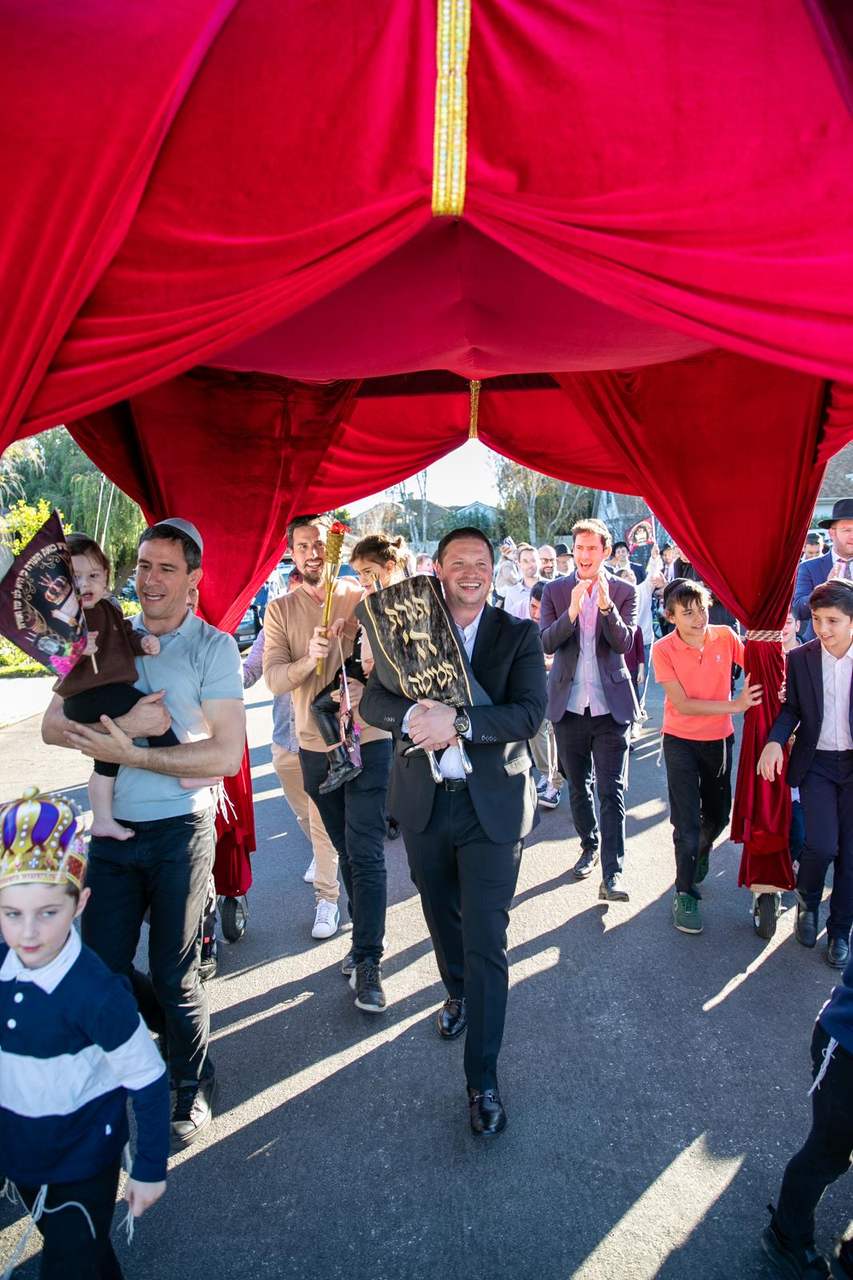 The Sefer Torah carried under a chuppah through the street, surrounded by dancing